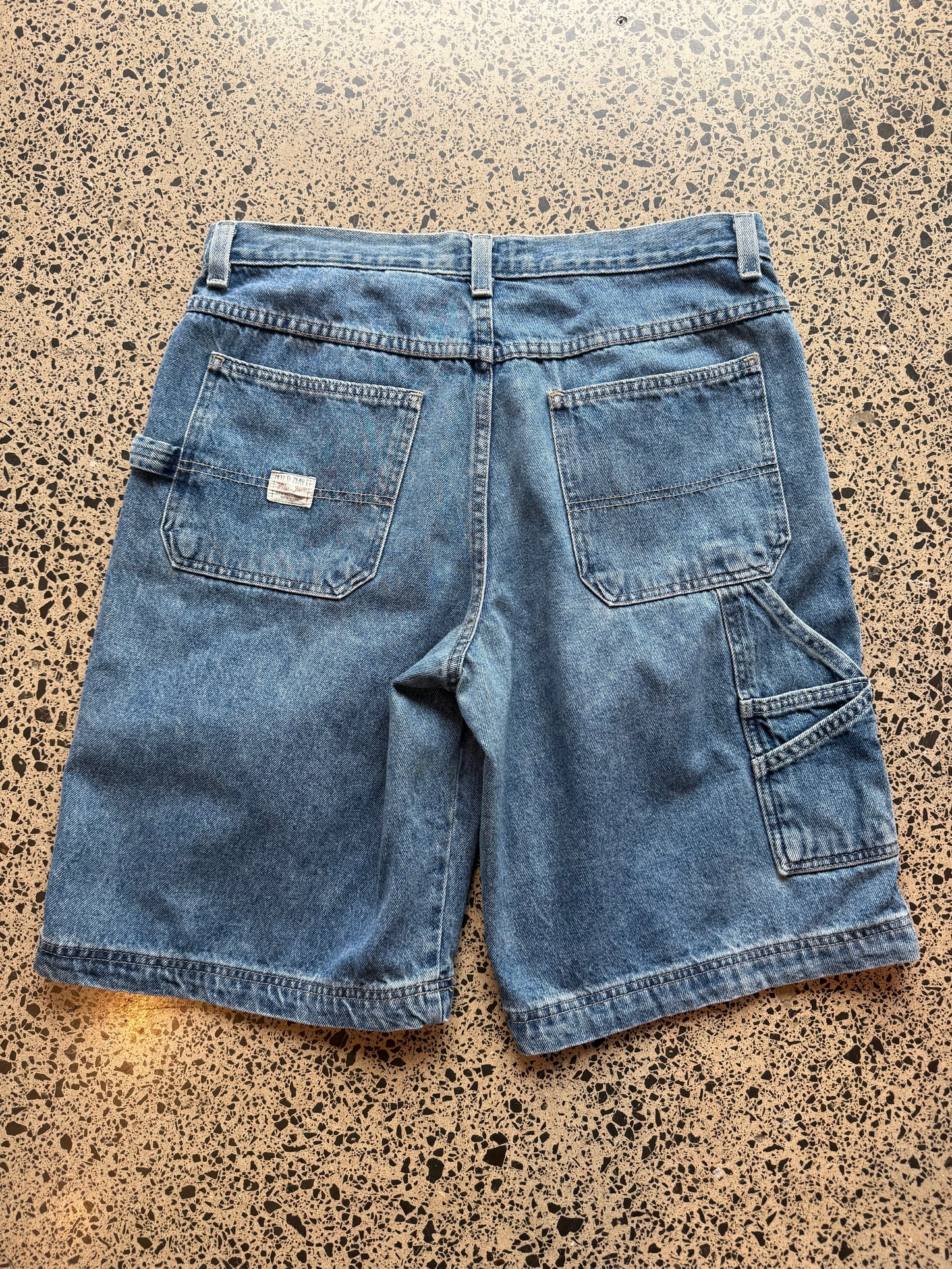 Old Navy dark blue wash denim jorts, size 34W, laid on polished concrete background. Knee cut with classic stitching and soft wash