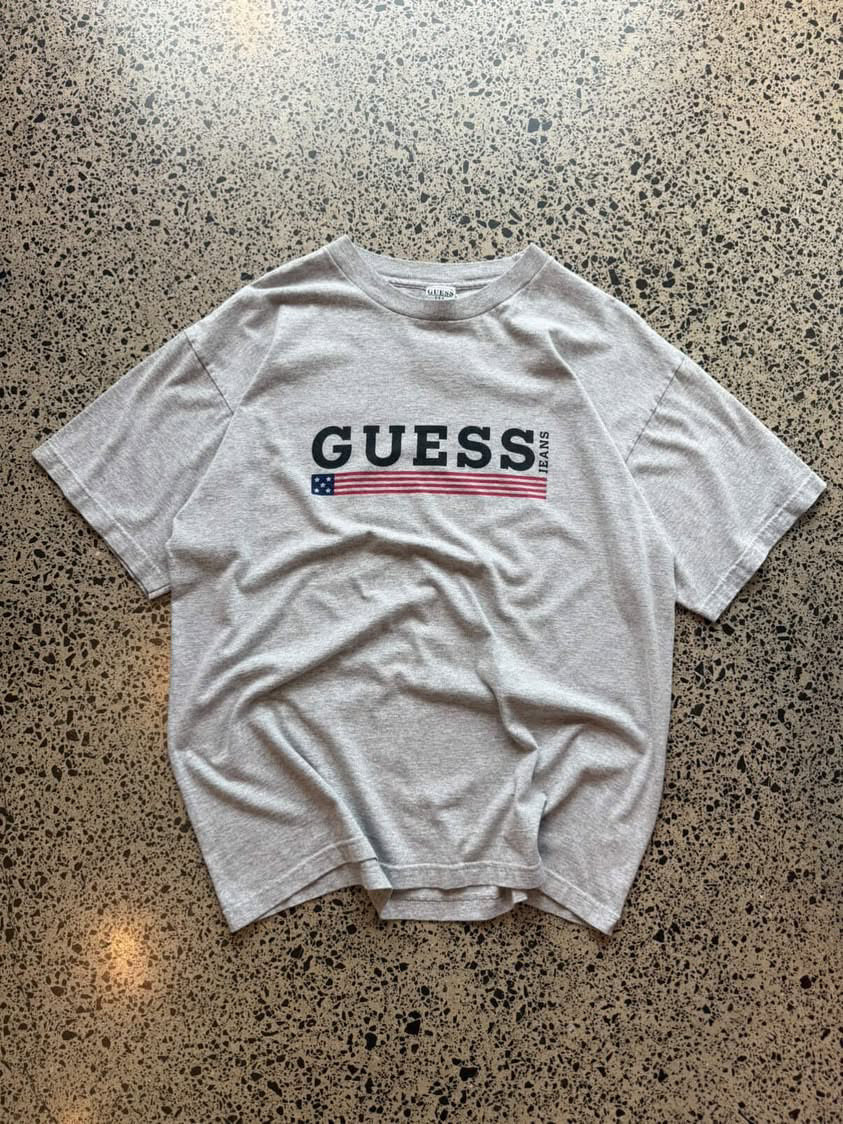90s Guess Jeans graphic T-shirt in size XL laid flat on a polished concrete background featuring classic logo branding.