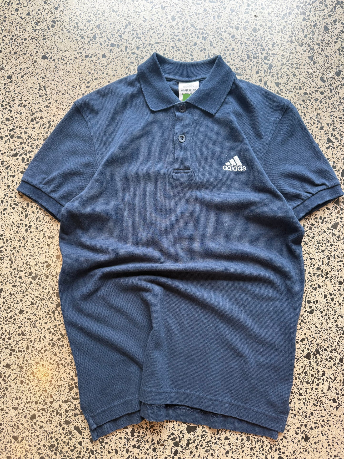 2000s Adidas polo shirt in size S laid flat on a polished concrete background featuring classic Adidas branding and a collared design.