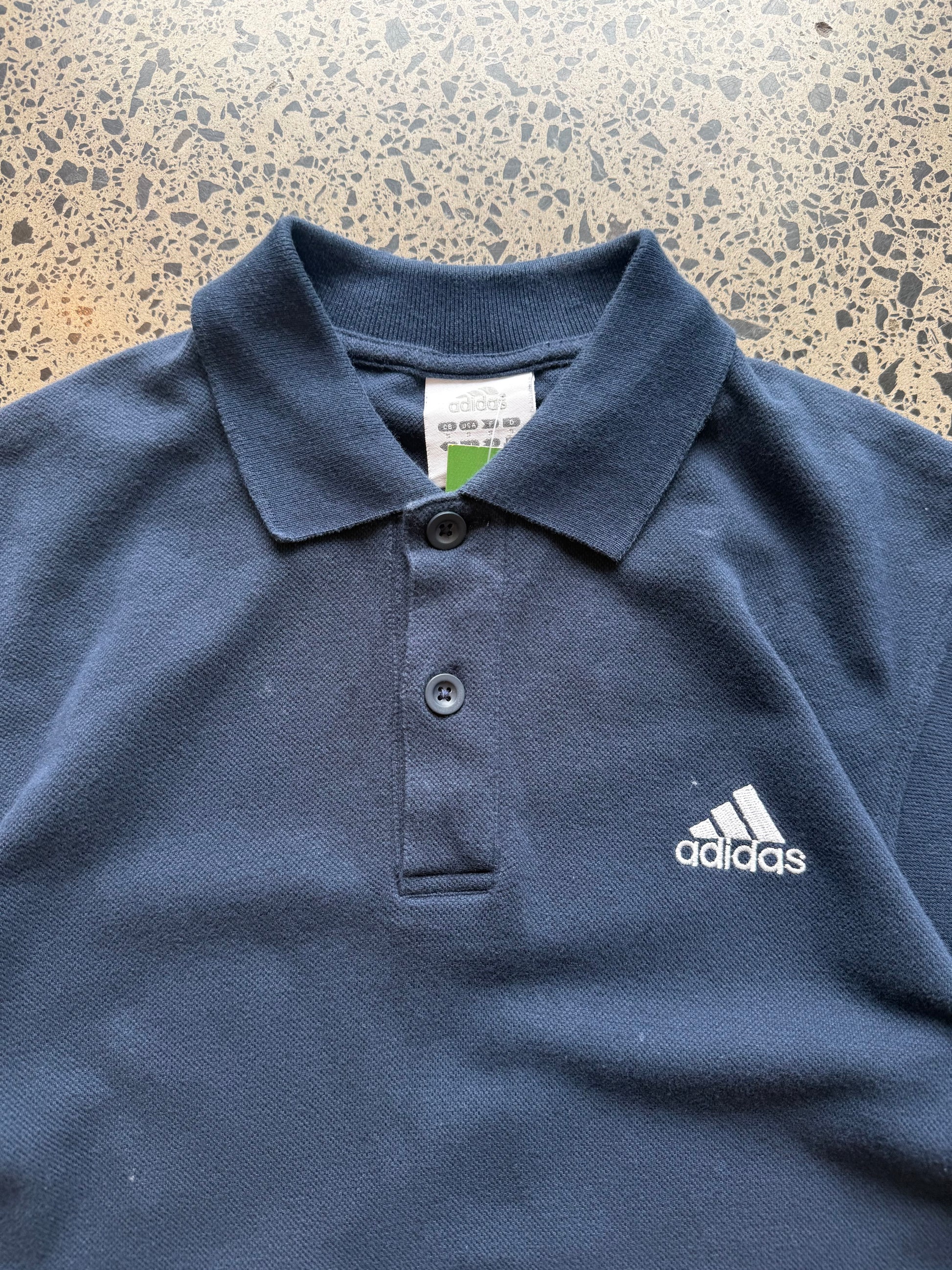 2000s Adidas polo shirt in size S laid flat on a polished concrete background featuring classic Adidas branding and a collared design.