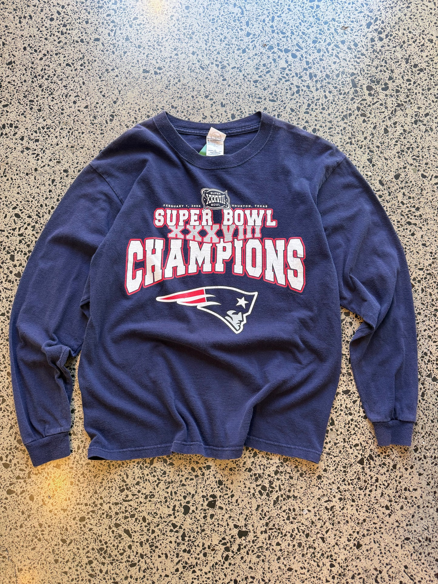 2004 New England Patriots Super Bowl Champions long sleeve shirt M laid flat on polished concrete background, vintage NFL tee with championship graphics and team branding.