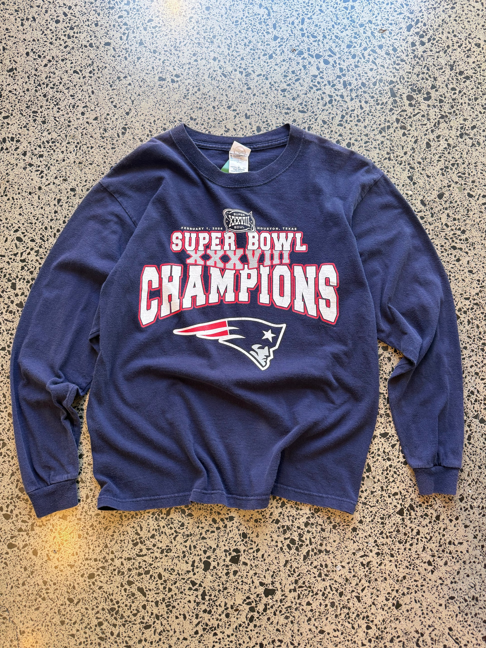 2004 New England Patriots Super Bowl Champions long sleeve shirt M laid flat on polished concrete background, vintage NFL tee with championship graphics and team branding.
