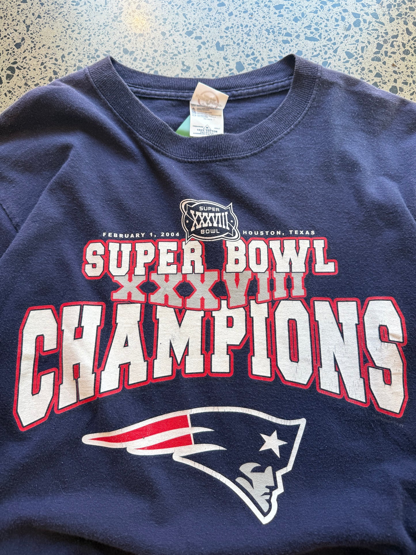 2004 New England Patriots Super Bowl Champions long sleeve shirt M laid flat on polished concrete background, vintage NFL tee with championship graphics and team branding.