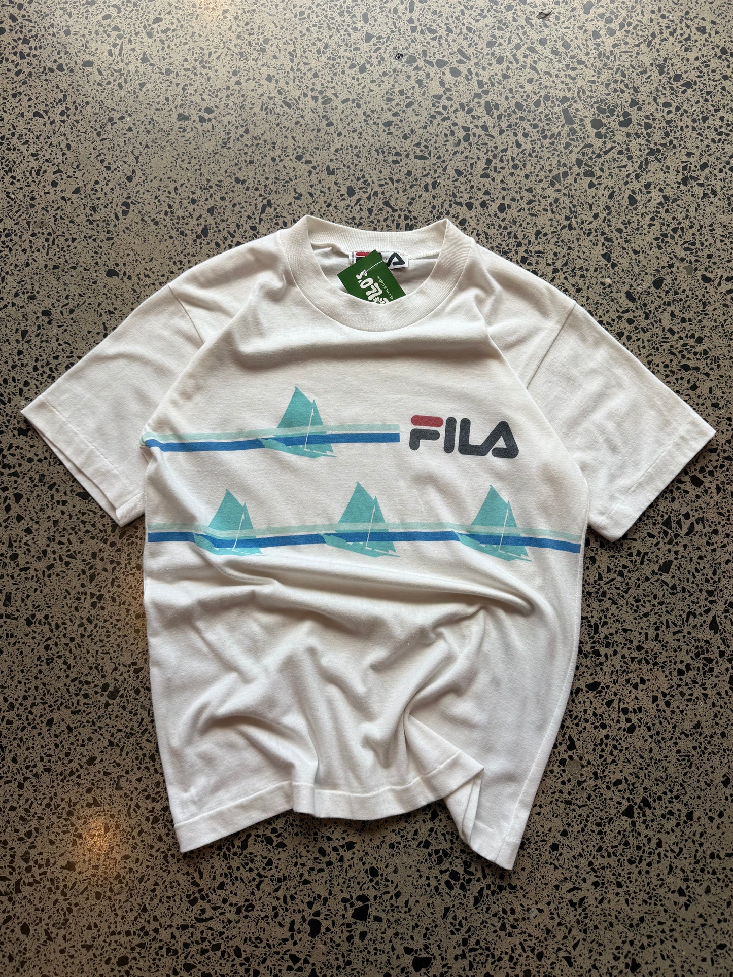 90s Fila graphic T-shirt, size L, laid on polished concrete background — vintage cotton tee with bold Fila logo print.