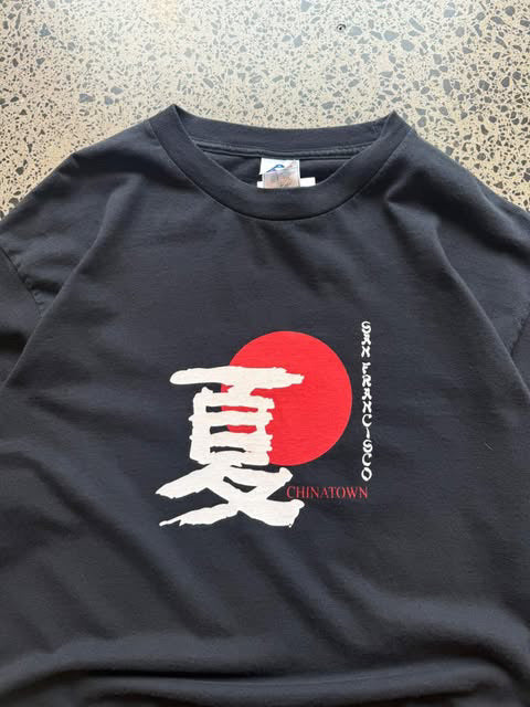 Early 2000s San Francisco Chinatown graphic T-shirt laid on a polished concrete background featuring a souvenir-style city graphic.