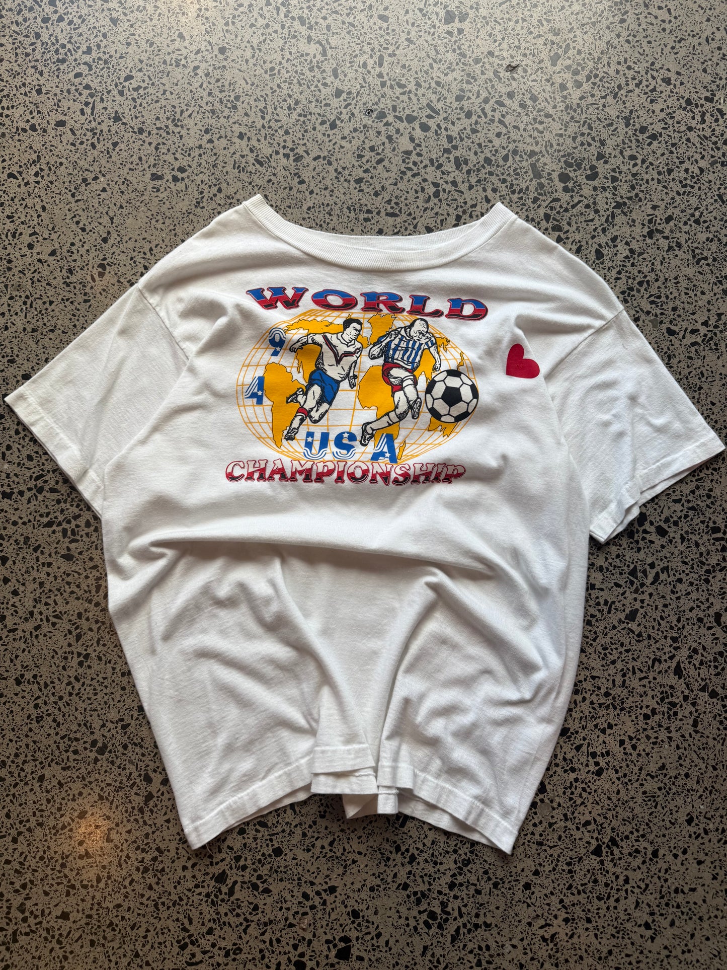 1994 USA World Champs football T-shirt, size L, laid on polished concrete background — vintage red, white, and blue sports graphic on soft cotton.