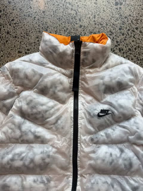 Reversible orange and white Nike jacket laid flat on a polished concrete background featuring classic Nike branding and dual-colour design