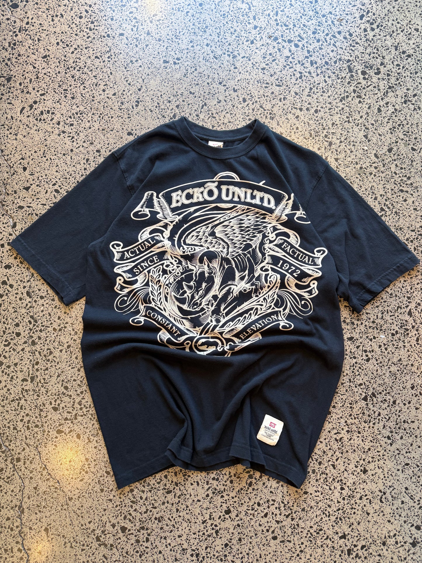 Ecko Unltd black graphic T-shirt size XL laid on polished concrete background — bold Y2K-style print on soft black cotton.